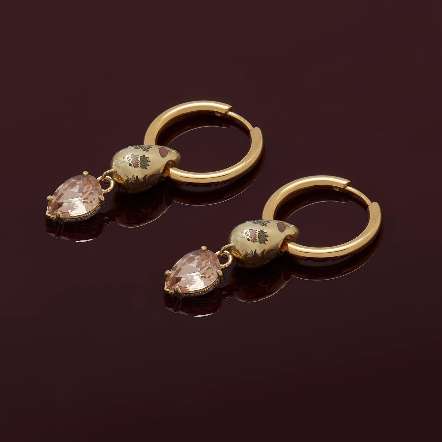 Pair of gold hoop earrings with teardrop-shaped gemstones on a dark background