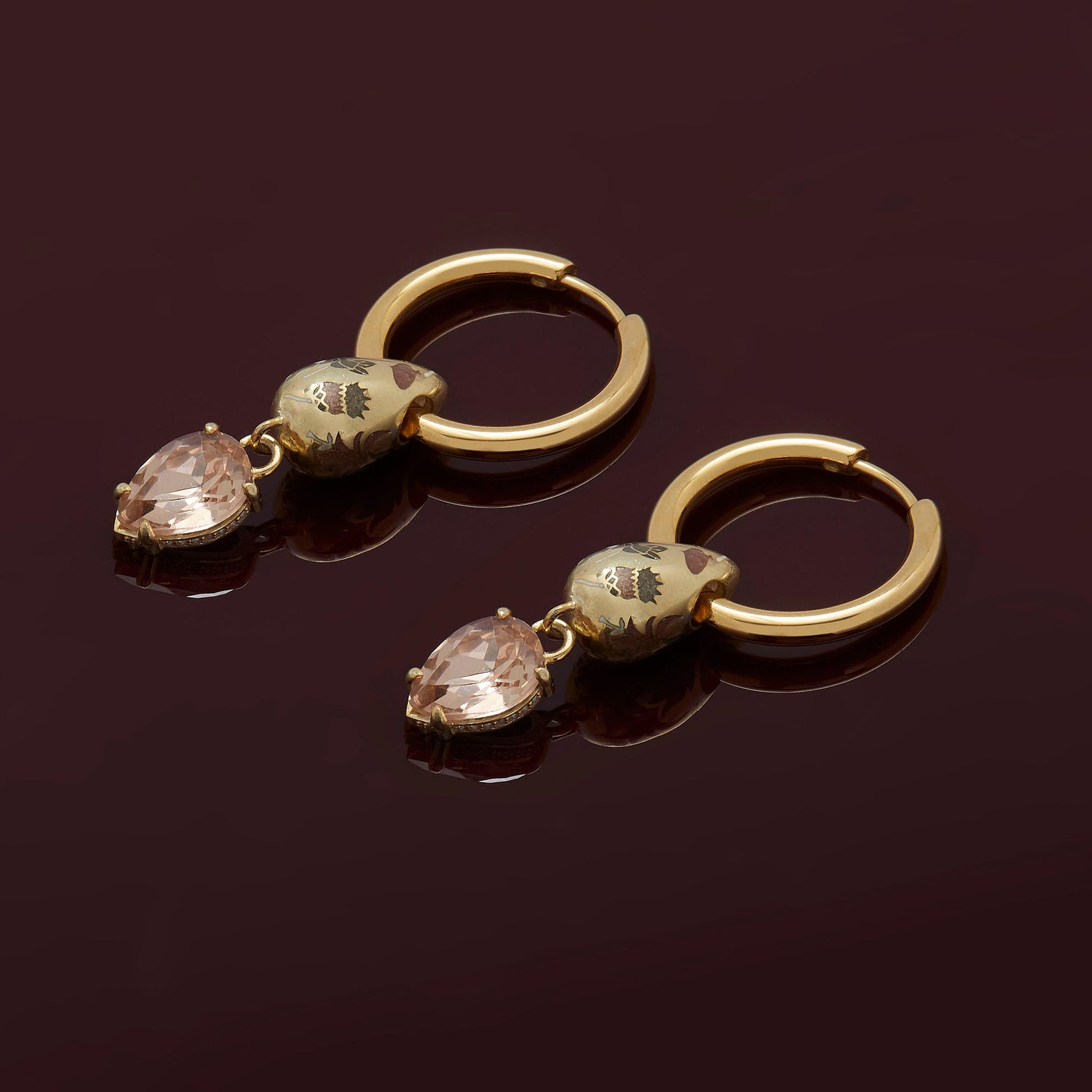 Pair of gold hoop earrings with teardrop-shaped gemstones on a dark background