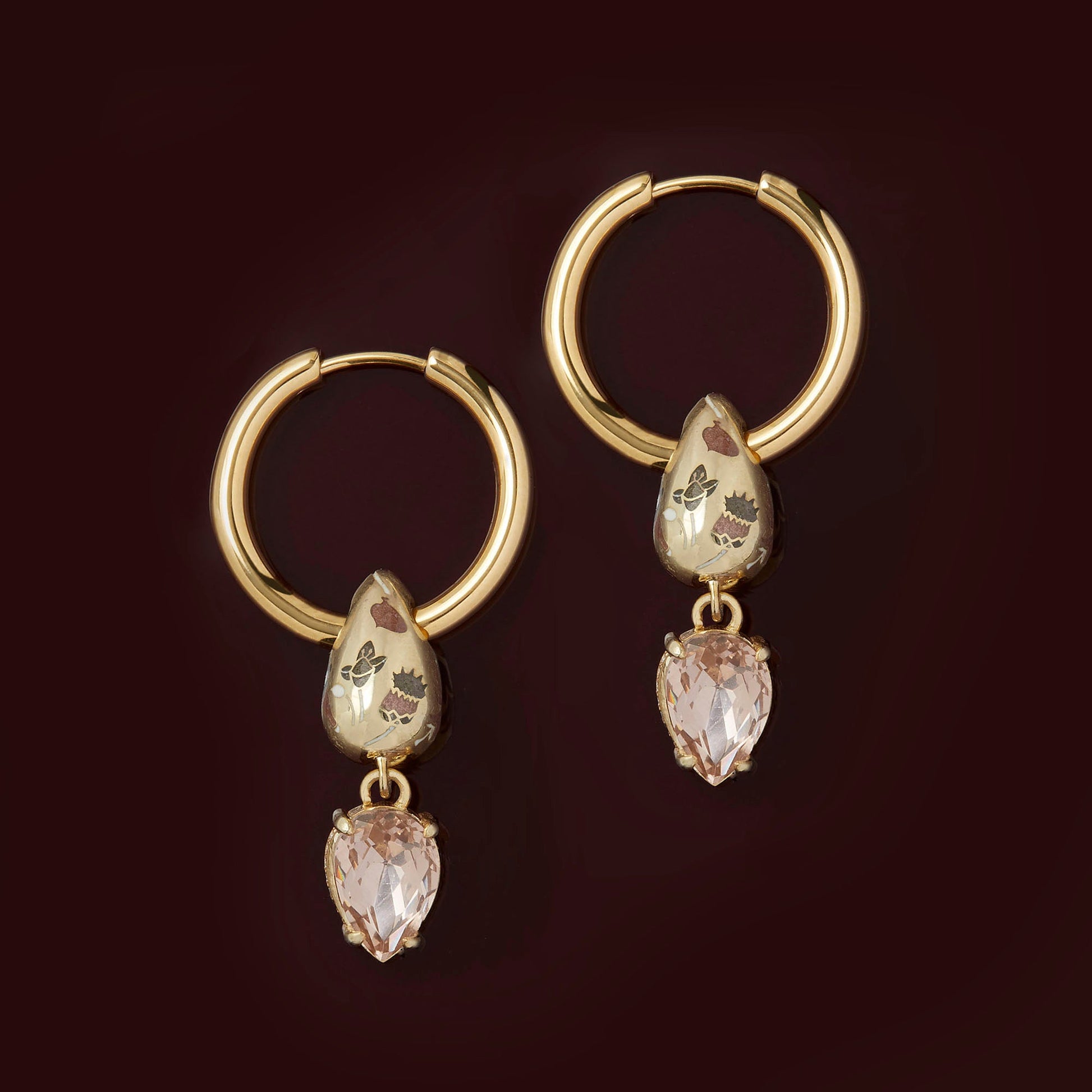 Gold hoop earrings with teardrop-shaped gemstones on a dark background