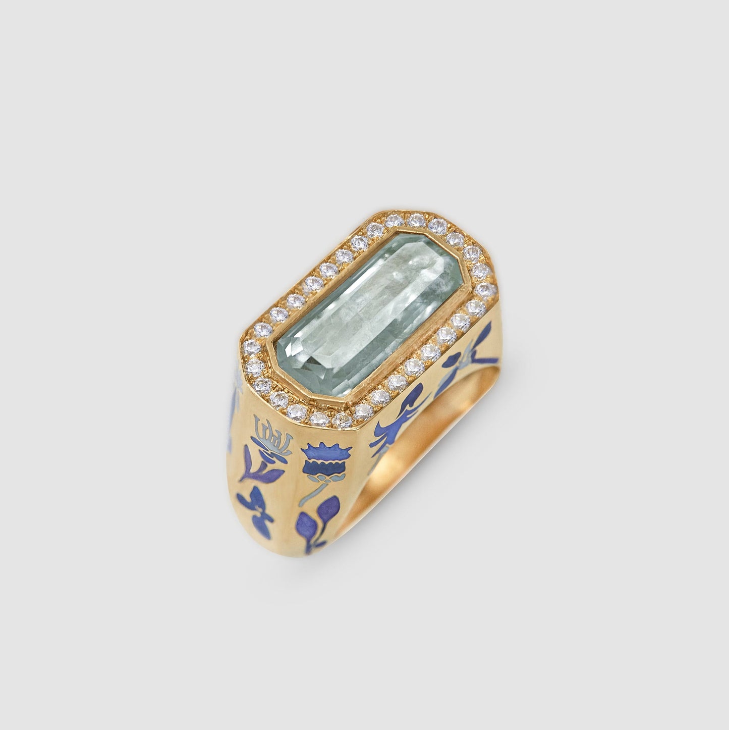 Gold ring with blue floral design and green gemstone on a light gray background